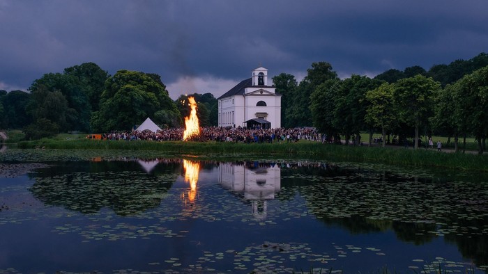 En lystgård med folk og tænder ved en sø ved aften.