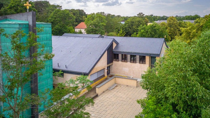 Ein modernes Gebäude mit blauer Fassade und dunklem Dach, umgeben von üppigem Grün und Bäumen.