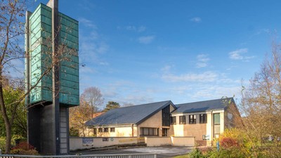 Modernes Gebäude mit grünem Turm und Parkplatz im Vordergrund