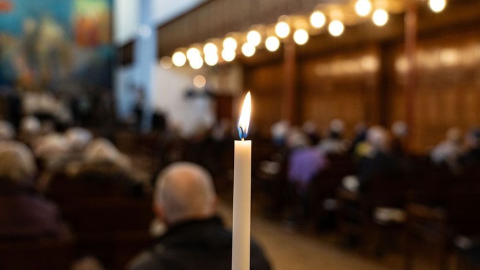 En lysende stearinlys i forgrunden, mennesker i kirke.