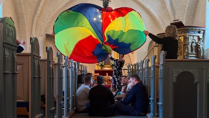 En far og barn sidder på bænke i kirke med en farverig paraply over dem