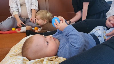 To børn spiller med legetøj på gulv, mens et nyfødt barn ligger på en dekke.