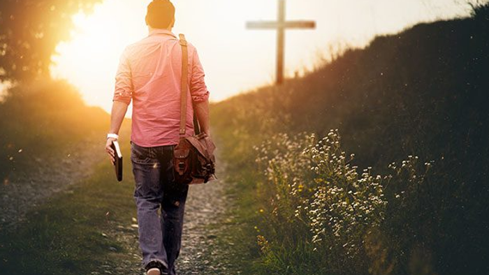 En mand går en sti med en rygpak og en bog i solnedgangens lys.
