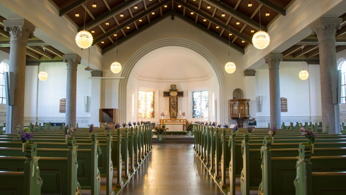 Indenrig af kirke med grønne bænke og hængende lygter