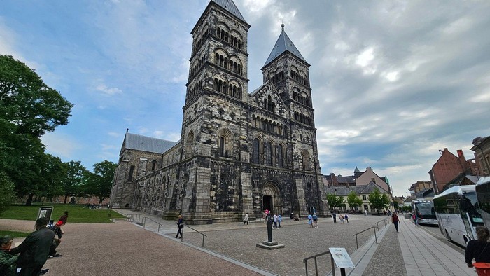 Historisk katedral med tvillingetårne placeret på en rummelig brostensplads, hvor besøgende udforsker.