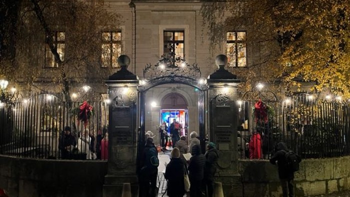 Nächtliche Szene vor einem Gebäude mit Menschenansammlung.