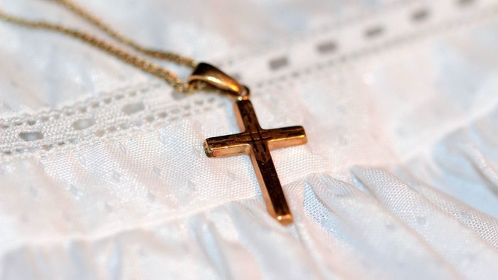 En guldkæde med et small cross hænger på et hvidt spandextrøje.