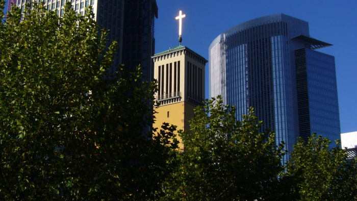 Hochhaus mit Kreuz und Bäumen im Vordergrund