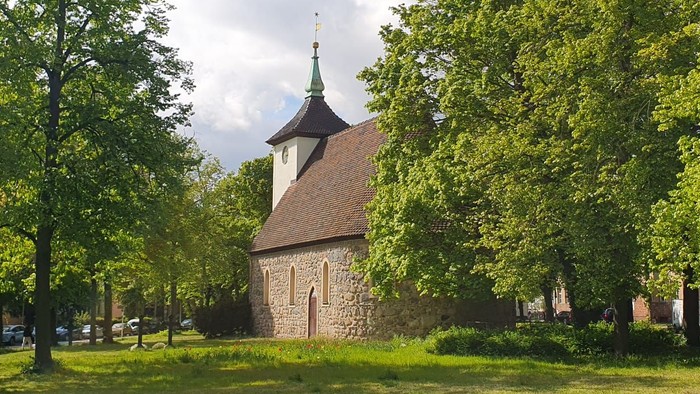 Historische Steinkirche, eingebettet zwischen üppigen grünen Bäumen in einer ruhigen, parkähnlichen Umgebung.