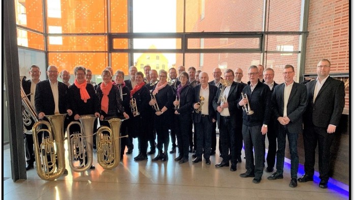 En gruppe mænd står sammen med blæserinstrumenter i et moderne lokal.