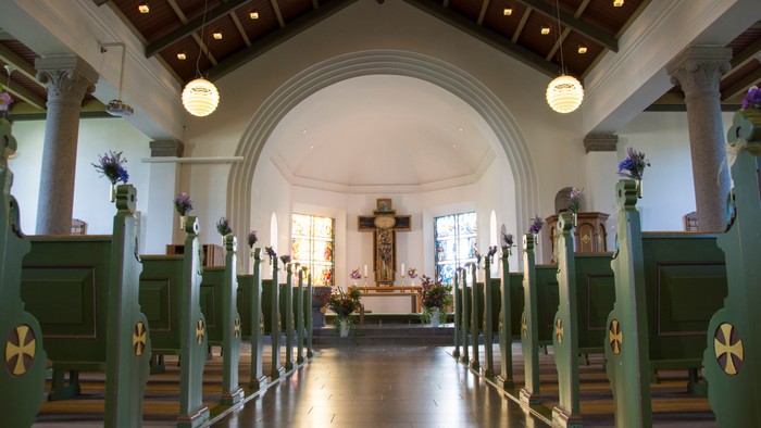Indre del af kirke med grønne bænke og alter i midten