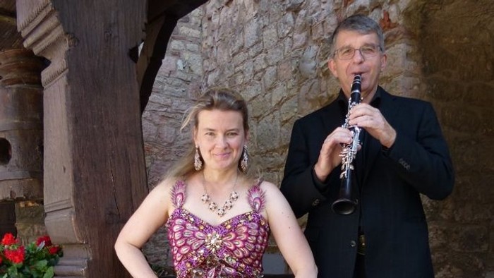 Frau in lila Kleid posiert neben einem Mann, der Klarinette und Akkordeon spielt.