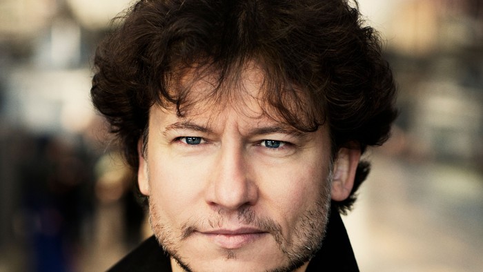 En mand med mørke hår og barbe, der bjerger en sort jakke og ser lige forud.