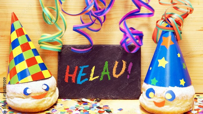 Luftschlagen über einem Schild, welches bunt beschriftet ist mit Helau! und 2 Kreppel mit Hütchen .