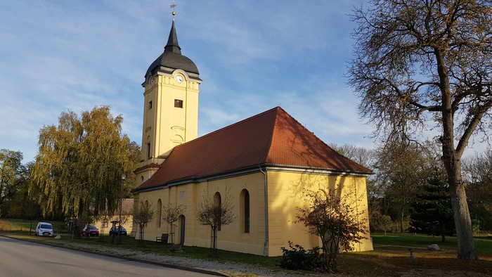 Kleine Kirche mit hohem Turm und rotem Dach neben Straße und Bäumen
