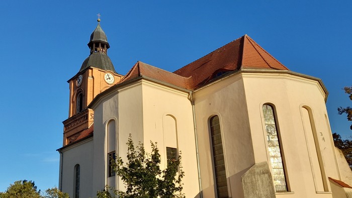 Kirchengebäude mit Uhrturm und rotem Dach unter blauem Himmel