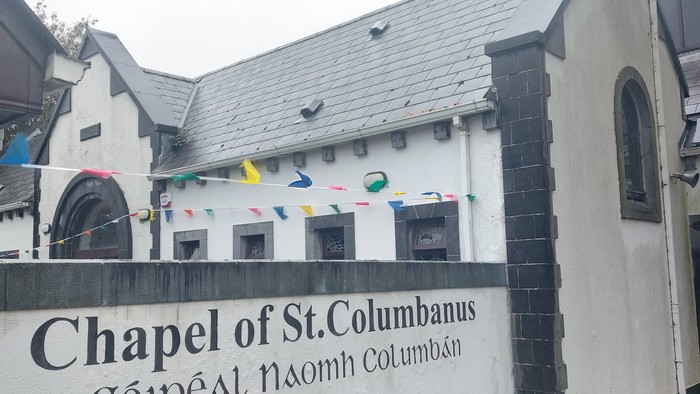 Die Kapelle des hl. Kolumbanus mit farbenfrohen Fahnen und Herbstlaub im Vordergrund