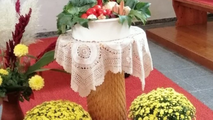 Ein Tisch mit verschiedenen Blumen, Gemüse und einer Vase, darauf ein Schild mit Segenswünschen