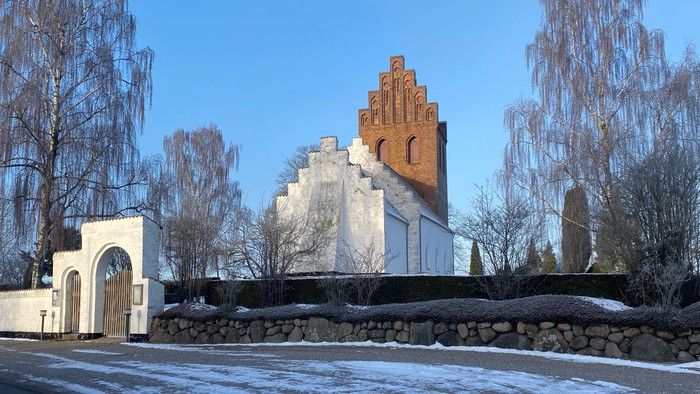 En lille kirke med tårn og mursten i en snedækked landsby.