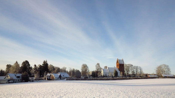 En snowy landsby med en kirke og huse under et klart blå himmel.