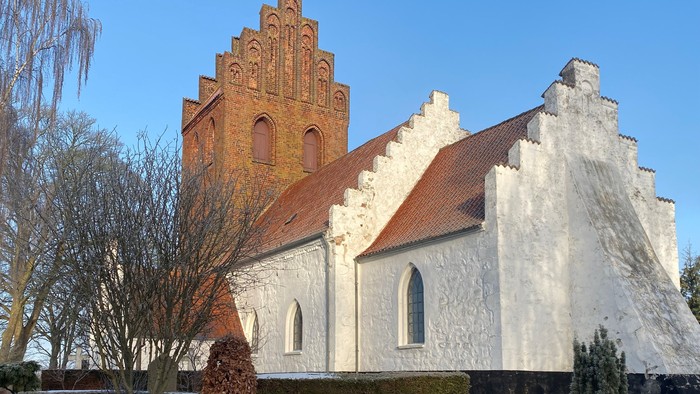 Hvid kirke med rødt tag og højt tårn.