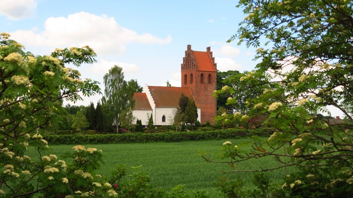 En rød kirke med tårn i grønne omgivelser
