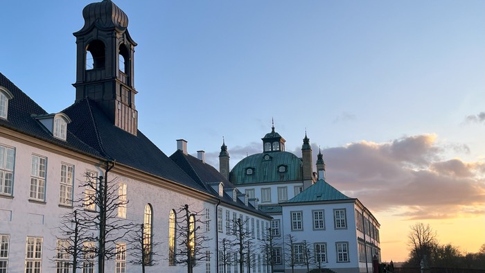 Stor historisk bygning med tårn og kuppelsaler ved solnedgang