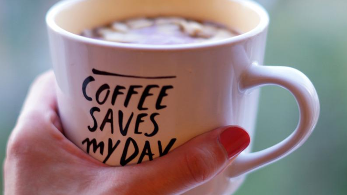En hånd holder en kaffekop med teksten 