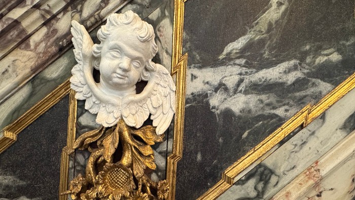 Udsmykket marmorrækværk med en kerubskulptur og gyldne dekorative elementer.