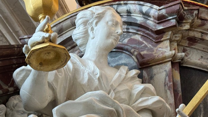 Kompliceret marmorstatue, der holder et gyldent bæger og er draperet i flydende gevandter.