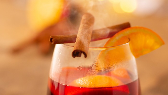 En glas med rød drik med en stokke kanel og en appelsinskive.
