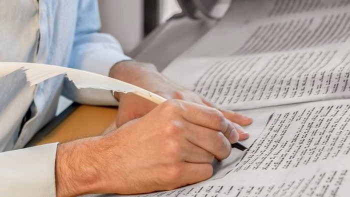 Hände halten aufgeschlagene Schriftrolle mit hebräischer Schrift