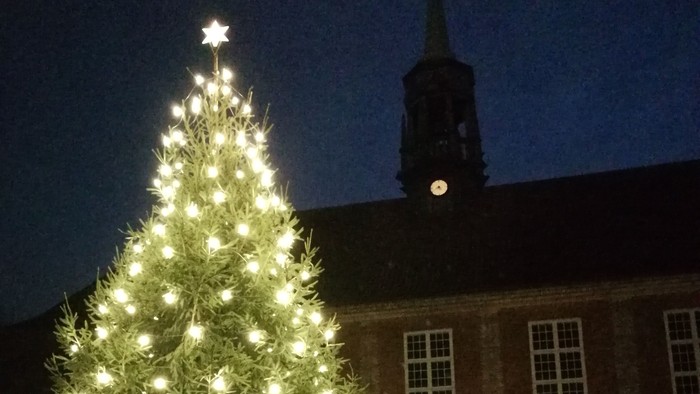 En stor juletree med lys foran kirke