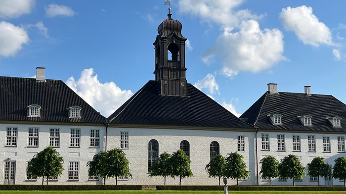 Det store slotte med klokketårn og grønne træer foran