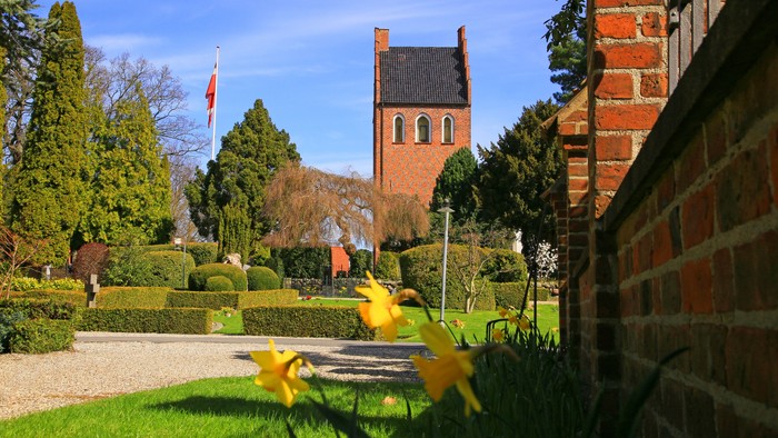 En smuk have med blomster, en mur og en kirke i baggrunden