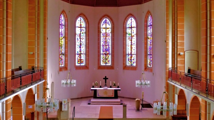 Innenraum einer Kirche mit Altarraum und farbigen Fenstern