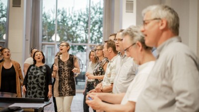 En gruppe af mennesker synger i et lys og rummeligt lokal.