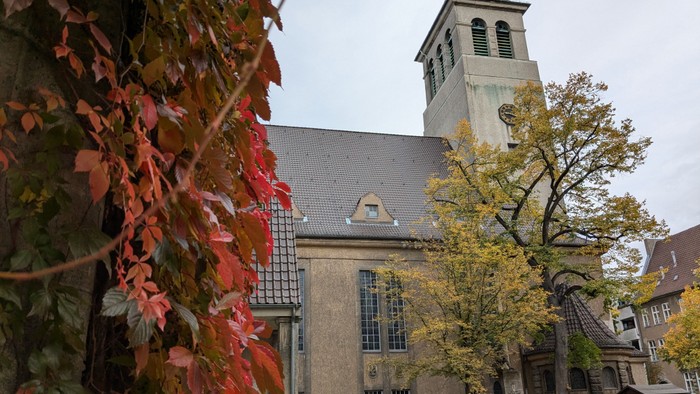 Kirchturm mit Uhr und Herbstlaub im Vordergrund