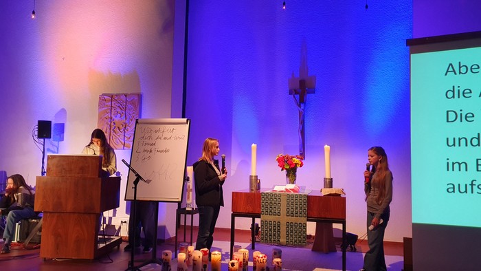 Eine feierliche Zeremonie mit Rednern, Kerzen und einer projizierten Botschaft in einem gut beleuchteten Innenraum.