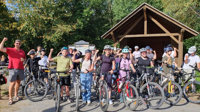 Eine Gruppe von Radfahrern mit Helmen posiert stolz mit ihren Fahrrädern in einer malerischen Outdoor-Umgebung.