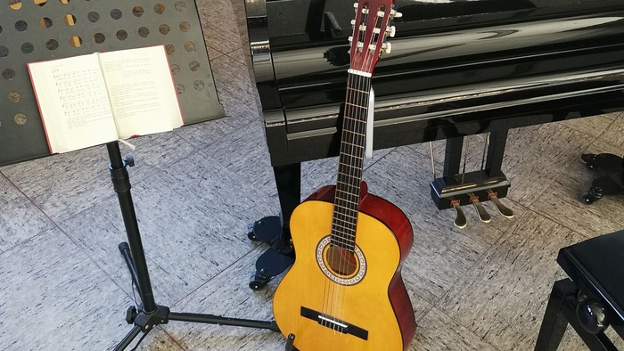 Auf dem Bild sind Gitarre, Notenständer und Klavier zu sehen. 