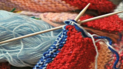 En rulle blå garn og en del ufuldstændige stråke, liggende på et stykke ufuldendt stråkearbejde