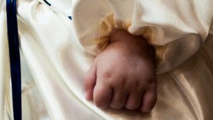 Et spæd barns hånd stikker ud af en hvid pude.