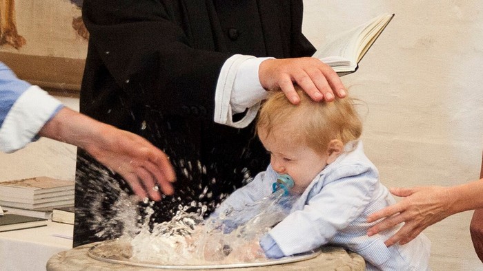 En præst børster en lille drengs hoved med vand i en kirke.