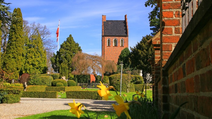 En smuk have med blomster, en mur og en kirke i baggrunden