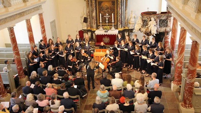 Et kor optræder i en stor kirke med et opmærksomt publikum siddende foran dem.