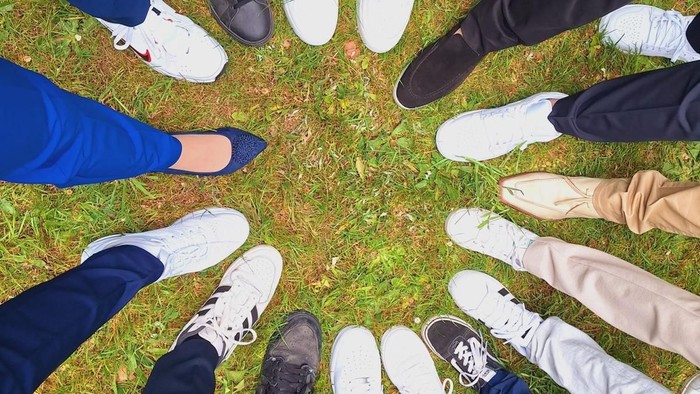 Eine Gruppe von Menschen, die eng beieinander auf Gras stehen und vielfältige Schuhwahl präsentieren.