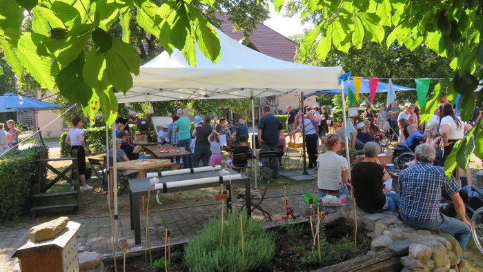 Ein belebter Freiluftmarkt mit vielen Menschen und bunten Markisen unter grünen Bäumen.