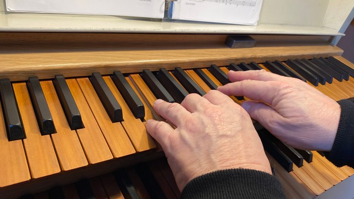 Hænder spiller på et piano med noter på stand.