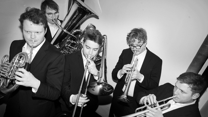 En gruppe musiker spiller blæsere i en koncertsal